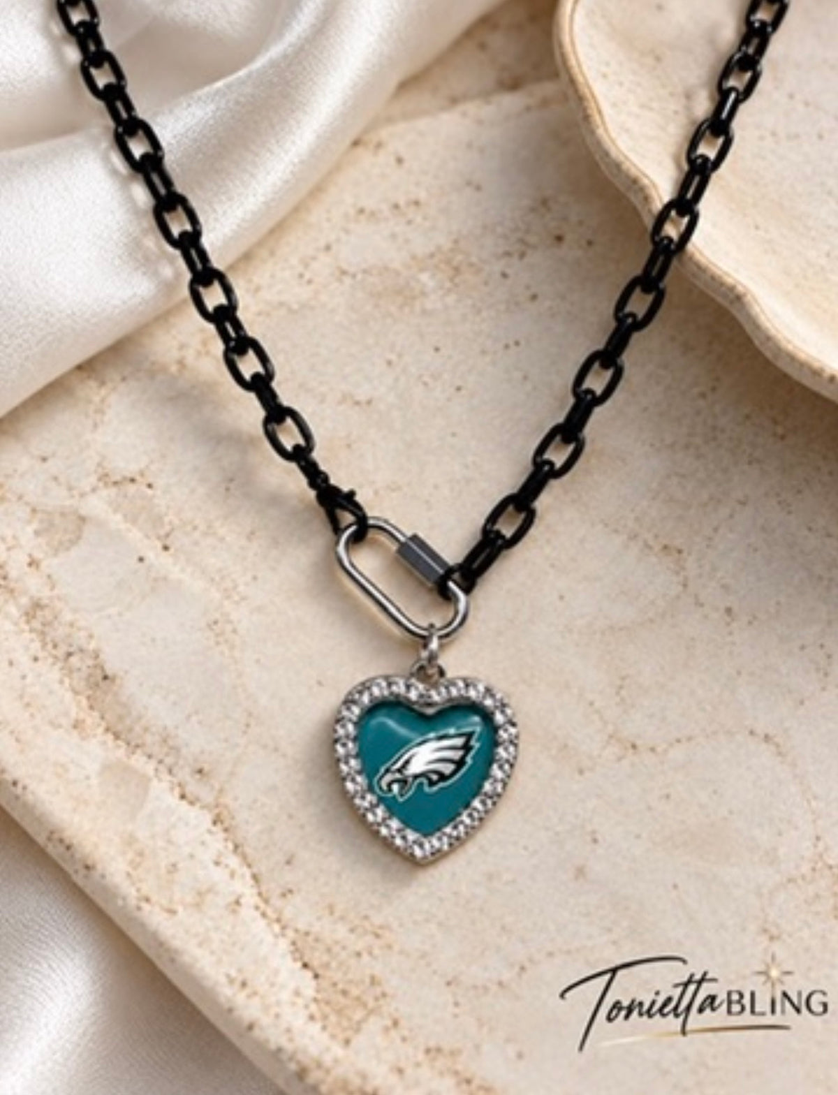 Black chain necklace with a carabiner clasp and a rhinestone-edged teal heart pendant with an eagle emblem