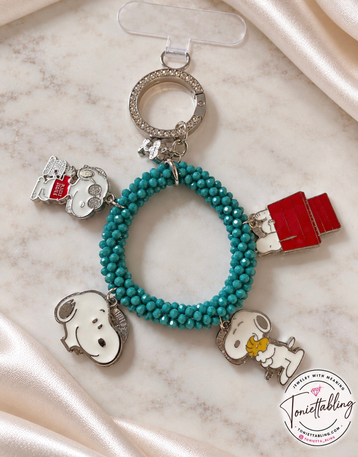 Teal beaded phone wristlet with a rhinestone ring clasp and Snoopy charms including Joe Cool, the red doghouse, and Snoopy hugging Woodstock
